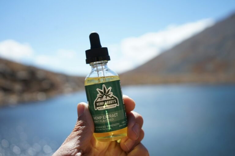 Hand holding Hemp Daddy’s hemp extract oil bottle outdoors near a lake