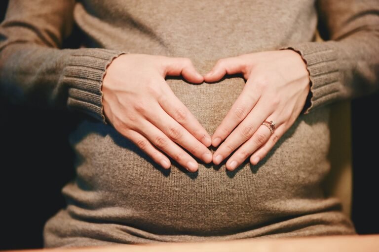 Pregnant woman making a heart shape on her belly with hands.