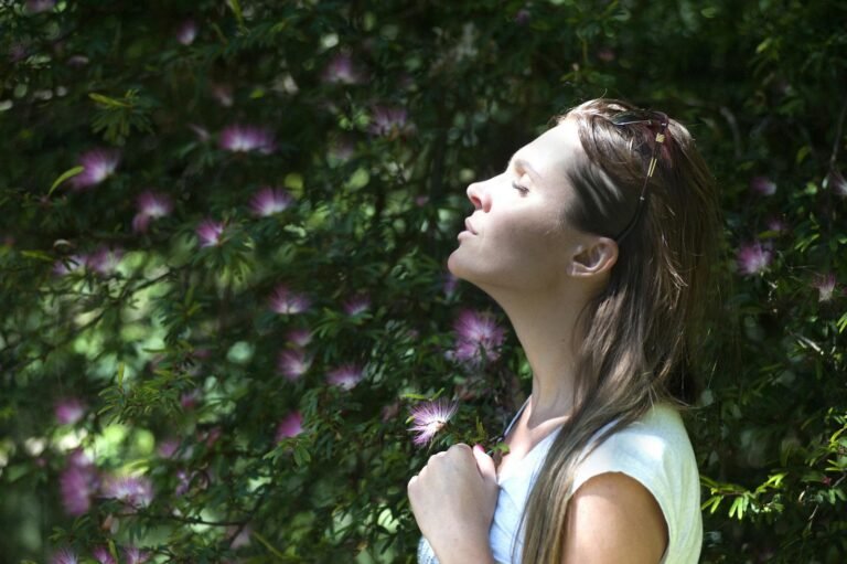 Woman standing outdoors with eyes closed, enjoying sunlight and nature