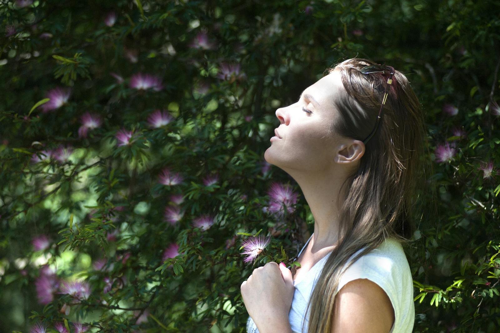 Woman standing outdoors with eyes closed, enjoying sunlight and nature