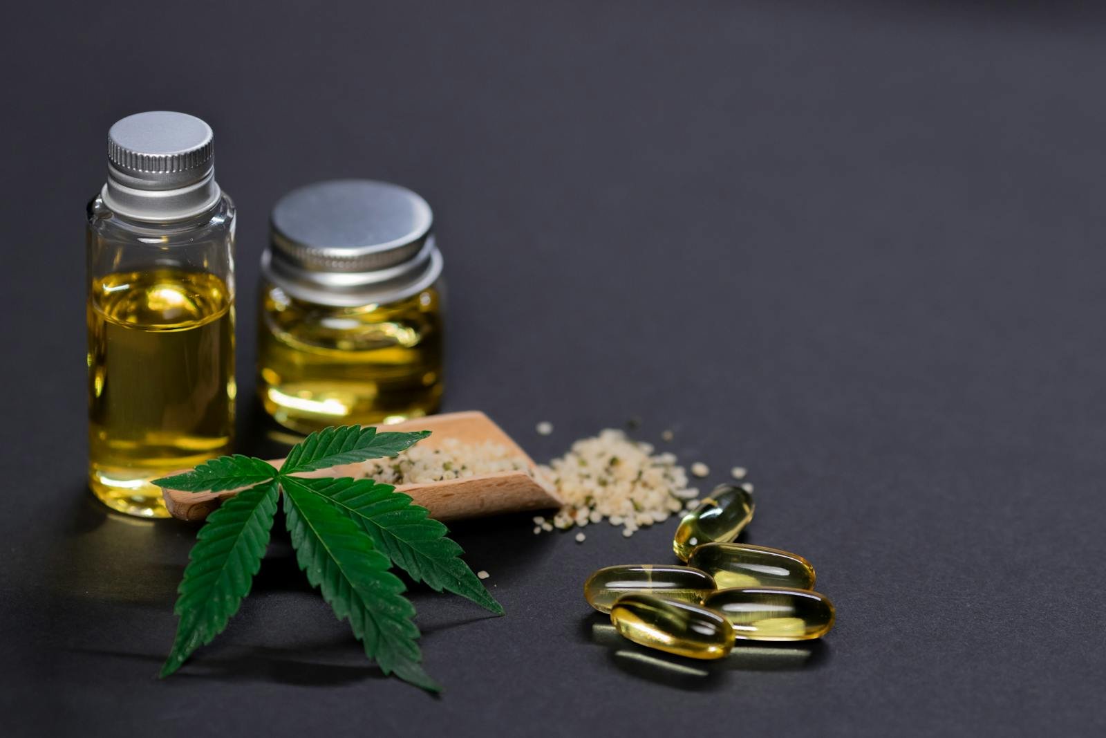 CBD oil bottles with capsules, hemp seeds, and cannabis leaf on dark background.