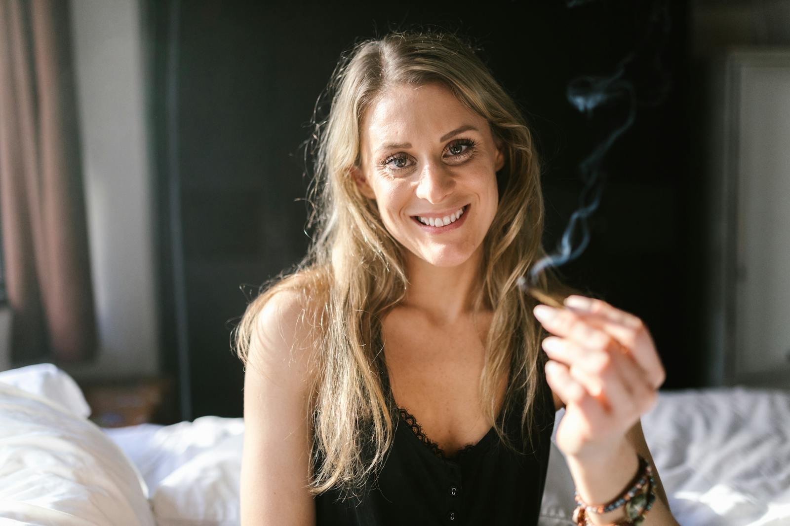 Smiling woman holding a smoking joint while relaxing indoors