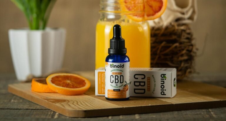 Binoid orange CBD wellness drops bottle with packaging and sliced oranges on wooden board