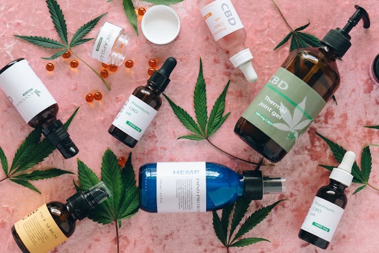 Flat-lay of assorted CBD products including oils, capsules, serum, and hemp gel with cannabis leaves