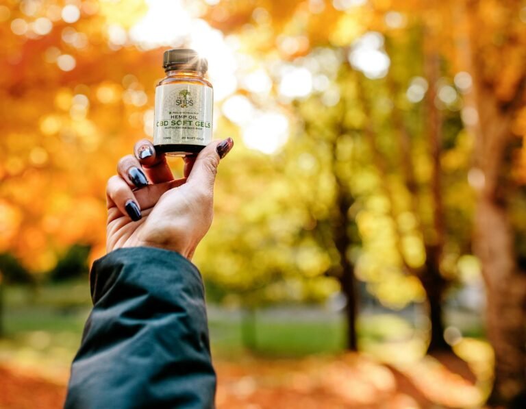 Hand holding hemp oil CBD softgels bottle outdoors with autumn leaves background