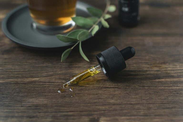 CBD oil dropper with golden liquid on wooden table next to a cup of herbal tea.