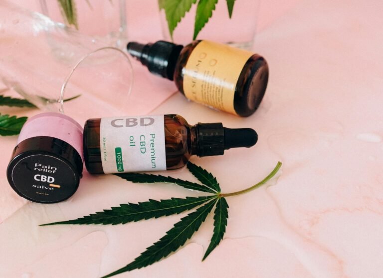 CBD premium oil dropper bottle, pain relief salve, and serum with hemp leaf on pink background