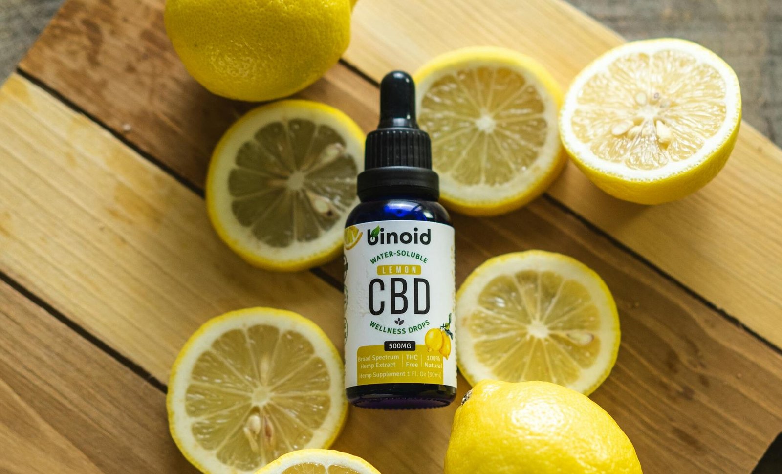 Binoid lemon CBD wellness drops bottle with sliced lemons on wooden board
